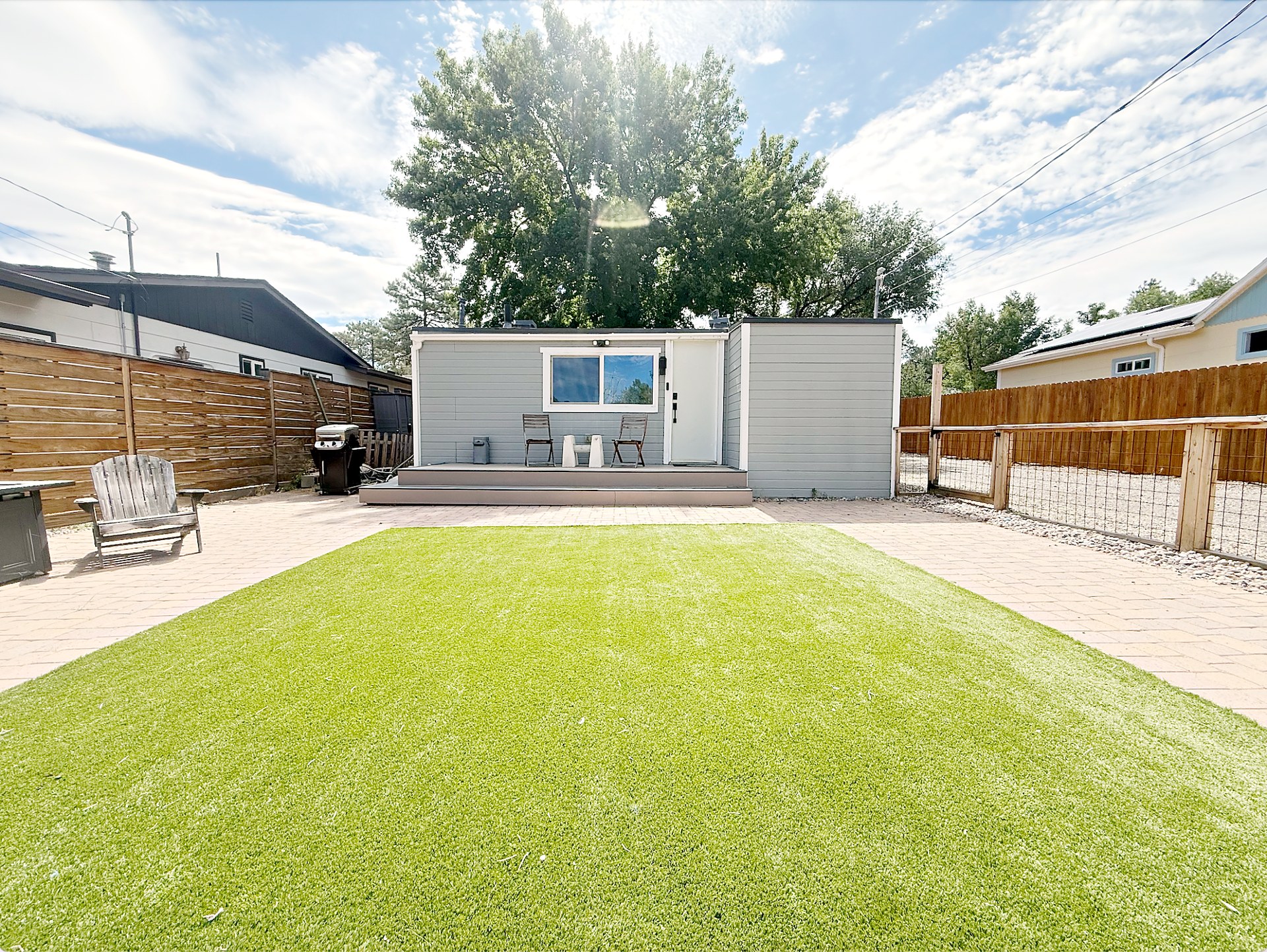 Fenced backyard with artificial grass lawn, pavers, and the tiny home under a blue Arizona sky
